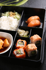 Japanese cuisine. Business lunch in a black box: rice, rolls, salad, sushi on a black table. Background image, copy space