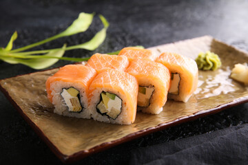 Japanese cuisine. Rolls philadelphia. Rice with red fish, avocado and cream cheese on a plate on a black table. Restaurant menu. Background image, copy space