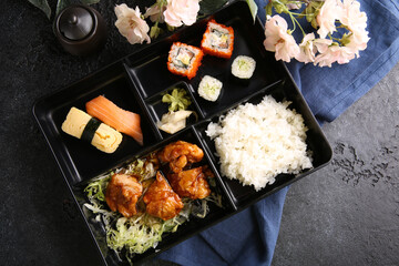 Japanese cuisine. Business lunch in a black box: rice, rolls, salad, sushi on a black table. Background image, copy space