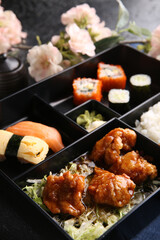 Japanese cuisine. Business lunch in a black box: rice, rolls, salad, sushi on a black table. Background image, copy space