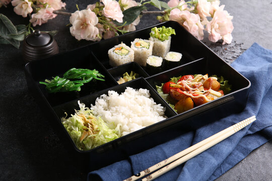 Japanese cuisine. Business lunch in a black box: rice, rolls, salad, sushi on a black table. Background image, copy space