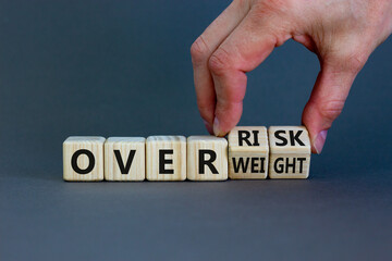 High risk from overweight symbol. Doctor turns wooden cubes and changes the words overweight to over risk. Beautiful grey background, copy space. Medical and high risk from overweight concept.