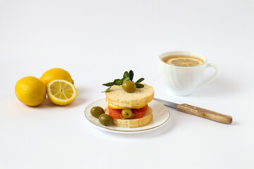 Sandwich with red fish, olives, lemon, three lemons, a knife and a tea mug on a white background, space for text