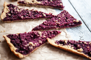 Pieces of delicious berry tart on parchment on a gray wooden background