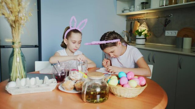 Little girls paints eggs. They draws Easter patterns on eggs.