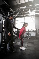 Vertical full length shot of a male personal trainer coaching his female client at the gym