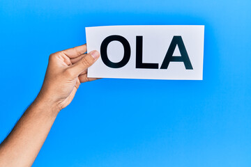 Hand of hispanic man holding ola word paper over isolated blue background.
