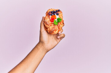 Hand of hispanic man holding sweet bun over isolated pink background.