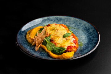 Chicken fillet baked in cheese with vegetable puree on a blue plate on a black background.