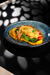 Chicken fillet baked in cheese with vegetable puree on a blue plate on a black background.