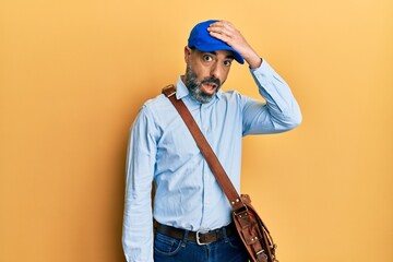 Middle age man with beard and grey hair wearing delivery courier cap surprised with hand on head...