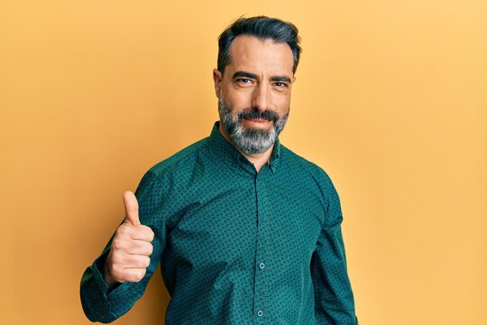 Middle age man with beard and grey hair wearing business clothes doing happy thumbs up gesture with hand. approving expression looking at the camera showing success.