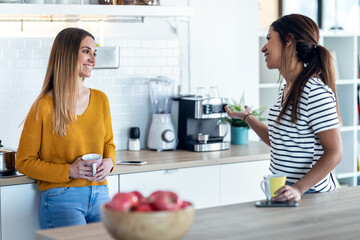 Two beautiful woman friends having breakfast and drinking coffee while talking in the kitchen at home.