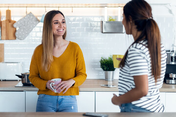 Two beautiful woman friends having breakfast and drinking coffee while talking in the kitchen at home.