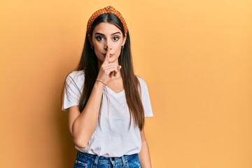 Beautiful brunette young woman wearing casual white t shirt asking to be quiet with finger on lips....