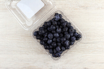 Square plastic container with blueberries on wooden background