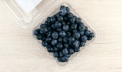 Blueberries in a plastic container on a wooden light background