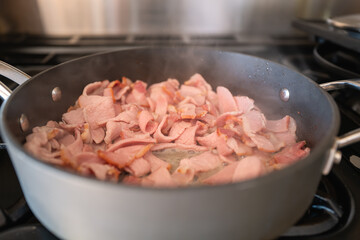 Chopped sliced bacon frying in a deep saucepan.