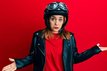 Hispanic young woman wearing motorcycle helmet clueless and confused expression with arms and hands raised. doubt concept.