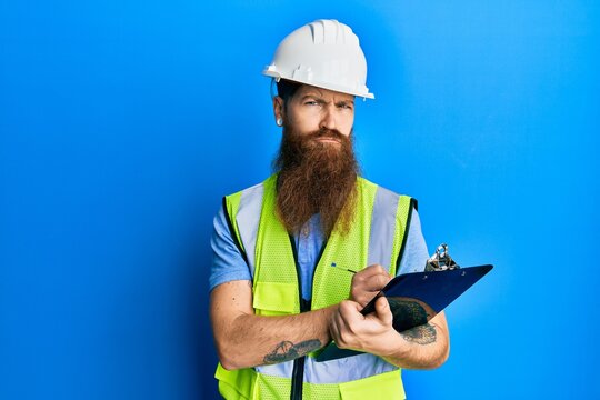 Redhead man with long beard wearing safety helmet holding clipboard depressed and worry for distress, crying angry and afraid. sad expression.