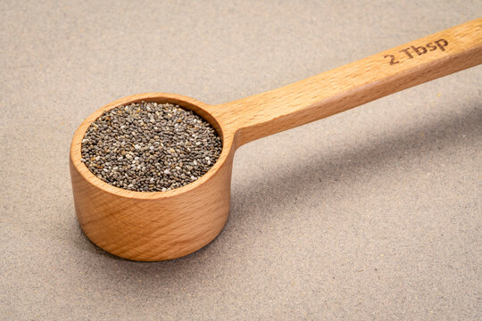 black chia seeds in wooden measuring scoop (2 tablespoons) against textured paper background, superfood concept