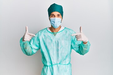 Young handsome man wearing surgeon uniform and medical mask looking confident with smile on face, pointing oneself with fingers proud and happy.