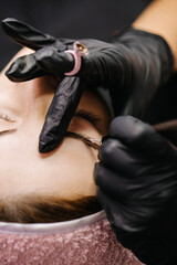 eyebrow microblading. A master in black gloves holds a blending needle over the brow of the model. Macro photography
