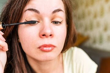 A young woman is doing makeup. Girl paints her eyelashes with mascara