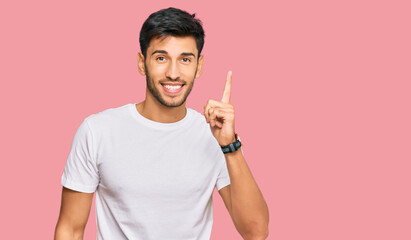 Young handsome man wearing casual white tshirt pointing finger up with successful idea. exited and...