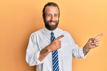 Handsome man with beard and long hair wearing business clothes smiling and looking at the camera pointing with two hands and fingers to the side.