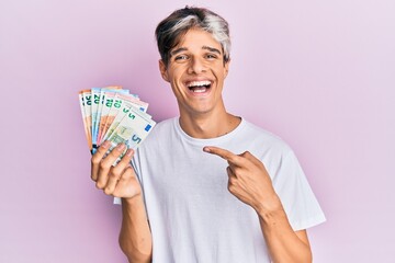 Young hispanic man holding euro banknotes smiling happy pointing with hand and finger