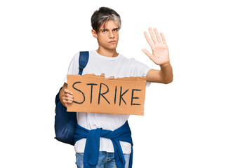 Young hispanic man holding strike banner cardboard with open hand doing stop sign with serious and confident expression, defense gesture