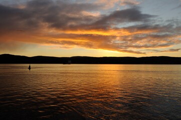 Obraz premium Autumn sunset in the city of Murmansk, late September. Dark mountains above the water, sunset, reflected in the water. Lonely buoy in the water. Murmansk region, Russia.