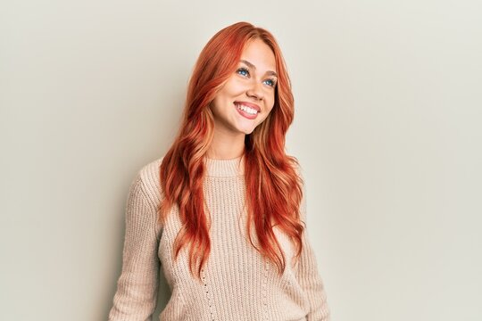 Young beautiful redhead woman wearing casual winter sweater looking away to side with smile on face, natural expression. laughing confident.