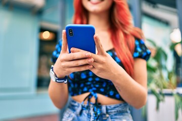 Young redhead girl smiling happy using smartphone at the city.
