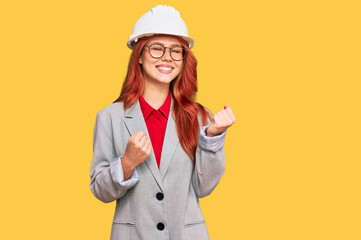 Young redhead woman wearing architect hardhat excited for success with arms raised and eyes closed celebrating victory smiling. winner concept.
