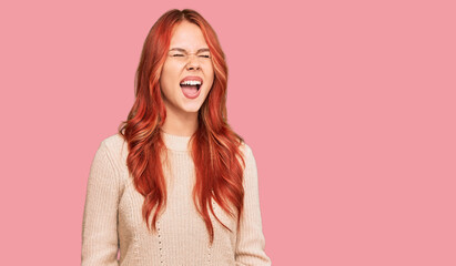 Obraz premium Young redhead woman wearing casual winter sweater angry and mad screaming frustrated and furious, shouting with anger. rage and aggressive concept.