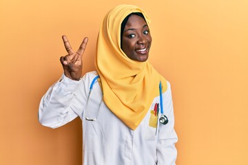 Beautiful african young woman wearing doctor uniform and hijab showing and pointing up with fingers number two while smiling confident and happy.