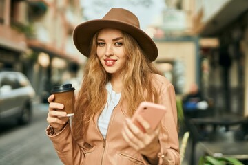 Young blonde girl using smartphone and drinking coffee at the city.