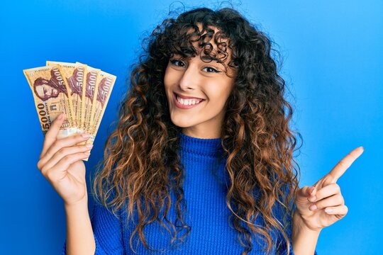 Young hispanic girl holding 5000 hungarian forint banknotes smiling happy pointing with hand and finger to the side