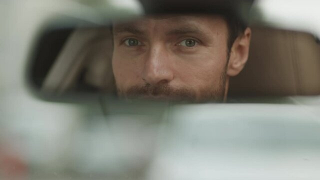Tracking left POV of Caucasian man looking and smiling on camera through car rear view mirror