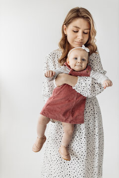 Young blonde mom holding a baby girl in her arms, mom with her daughter on a white background