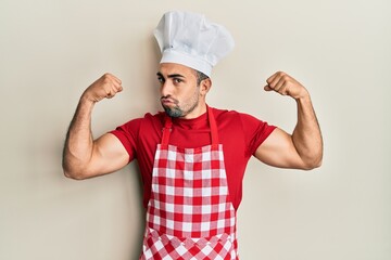 Young hispanic man wearing baker uniform showing arms muscles smiling proud. fitness concept.