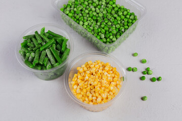 Plastic container with different organic deep frozen vegetables on a white concrete table