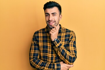 Young hispanic man wearing casual clothes looking confident at the camera smiling with crossed arms and hand raised on chin. thinking positive.