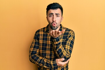 Young hispanic man wearing casual clothes looking at the camera blowing a kiss with hand on air being lovely and sexy. love expression.