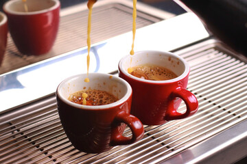two cups of coffee stand on the grill, coffee with foam poured from the coffee machine blurred background