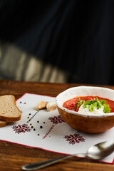 Borscht with sour cream in handmade ceramic bowl on wooden table. Contains bread, green onions, peppers and garlic. Traditional Ukrainian cuisine.
