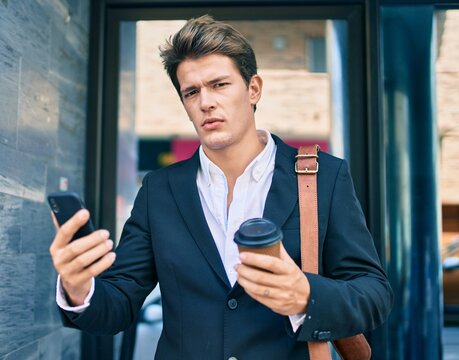 Young caucasian businessman with serious expression using smartphone and drinking coffee at the city.