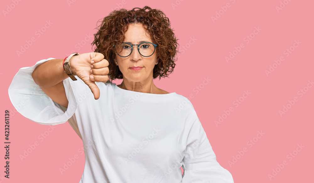 Wall mural Beautiful middle age mature woman wearing casual clothes and glasses looking unhappy and angry showing rejection and negative with thumbs down gesture. bad expression.